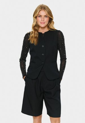 Black tailored vest features a round neckline, five buttons, with sheer black long sleeves adorned with silver embellishments, paired with matching shorts.