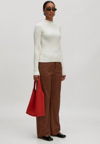 Weißer gestreifter Rollkragenpullover, braune weite Hose, rote Tragetasche, schwarze Schuhe, runde Sonnenbrille und blaue Ohrringe.