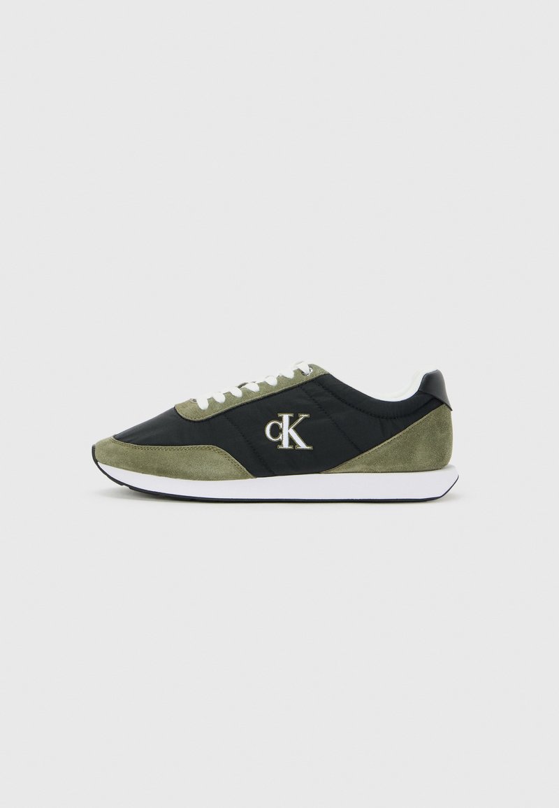 Zwarte en olijfgroene sneaker met witte veters en zool, met een "cK" logo aan de zijkant, getoond vanaf de zijkant op een effen achtergrond.
