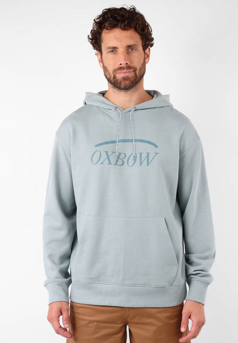 Hoodie bleu clair avec une poche avant et un cordon de serrage. Logo "Oxbow" en bleu plus foncé sur la poitrine. Texture de tissu douce.
