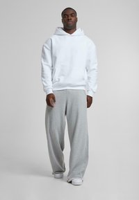 White hooded sweatshirt with a front pocket paired with light gray sweatpants. Both are made of soft, textured fabric. Casual, relaxed fit.
