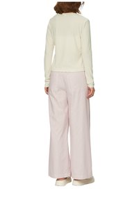 Helles beige Langarmshirt mit gerippter Textur, kombiniert mit hellrosa weit geschnittenen Hosen mit vertikalen Streifen und Gesäßtaschen.