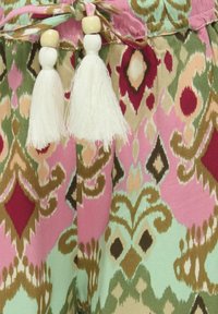 Barevná látka s velkým, složitým ikat vzorem v růžové, zelené a hnědé barvě. Obsahuje bílé třásně a dřevěné korálky na zavázání.