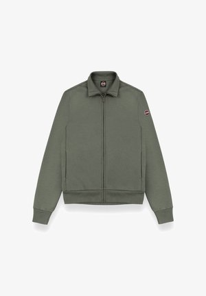 Zielona oliwkowa kurtka zapinana na zamek, wykonana z miękkiego materiału, z kołnierzem stojącym, ściągaczami na rękawach oraz okrągłym logo na lewym rękawie.