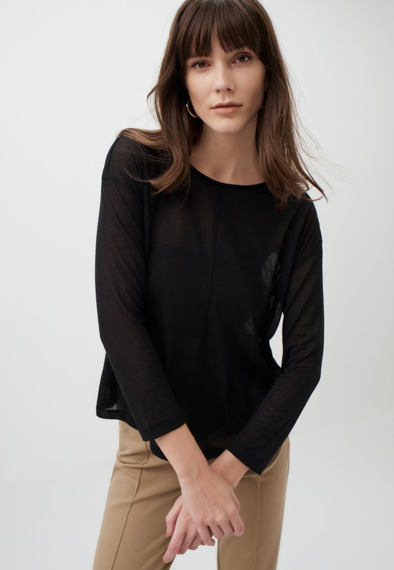 Zwarte langesleeve top van lichtgewicht, doorschijnend materiaal met een ronde hals en een comfortabele pasvorm, gecombineerd met een beige broek.