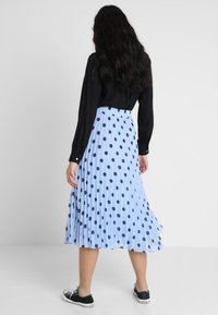 Gonna plissettata blu chiaro con pois neri. La fascia elastica offre comfort. Indossata con un top nero a maniche lunghe e sneakers nere.