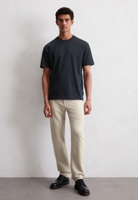 Granatowa koszulka z krótkim rękawem, gładka bawełniana tekstura, w połączeniu z jasnobeżowymi spodniami typu straight-leg i czarnymi sznurowanymi butami.