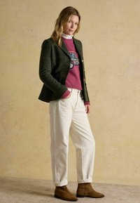 Vihreä ruudullinen bleiseri, vaaleanpunainen brodeerattu neuletakki, valkoiset housut, ruskeat nilkkurit, neutraalilla taustalla. Teksturoituja kankaita näkyvissä.