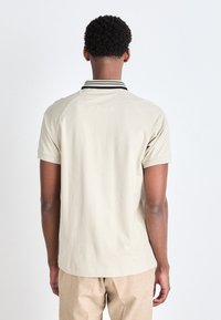 Beige polo shirt met korte mouwen, voorzien van een zwart-wit gestreepte kraag en een minimalistisch ontwerp. Zichtbare naden op de schouders en de achterkant.