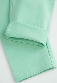 Jasnozielona bawełniana tkanina z zawiniętym mankietem. Materiał jest gładki z widocznym szwem wzdłuż krawędzi. Prosty i nowoczesny design.