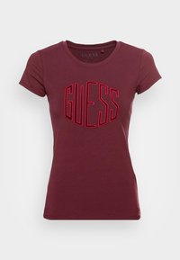 Kvinders tætsiddende kortærmet burgunder t-shirt med rødt "GUESS" logo broderet på fronten.