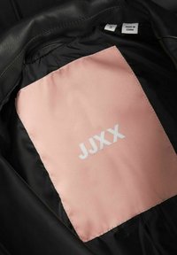 Veste noire avec une étiquette intérieure rose affichant "JJXX" et une étiquette de taille marquée "S" et "Made in China."