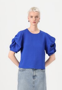 Short-sleeved blue top with puffed sleeves, textured fabric, round neckline, paired with a denim skirt.