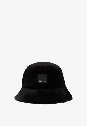 Chapeau seau noir en fausse fourrure douce, avec un large bord et une étiquette carrée noire portant un texte blanc indiquant "KARL LAGERFELD JEANS".