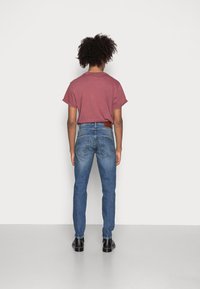 Camiseta de manga corta color burdeos combinada con jeans de mezclilla azul. Los jeans son ajustados, cuentan con una etiqueta de cuero marrón y dos bolsillos traseros. Zapatos negros.