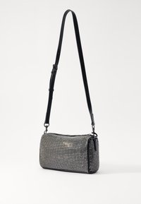 Svart cylindrisk väska med en texturerad yta som har små silvernitar, justerbar rem och dragkedjeöppning upptill.