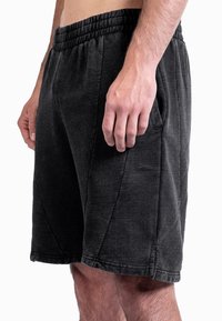 Calções desportivos pretos com cintura elástica, bolsos laterais e tecido macio e texturizado. Costuras reforçadas ao longo da bainha e das costuras.