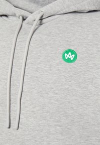 Felpa grigia con coulisse grigia chiara e un logo circolare verde con un design stilizzato. Tessuto morbido e texturizzato con una vestibilità rilassata.
