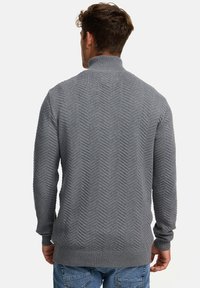 Grå strikket genser med høy krage, med fiskebensmønster og ribbestrikkede mansjetter og hem. Myk tekstur, uformell design.