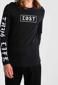 Black long-sleeve t-shirt made of cotton, featuring “LOST” logo in white on the front and “TRUE LIFE” text in white down the sleeves.