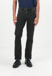 Jeans de mezclilla gris oscuro con corte recto, bolsillos frontales visibles y detalles cosidos, combinados con zapatos negros de cordones.