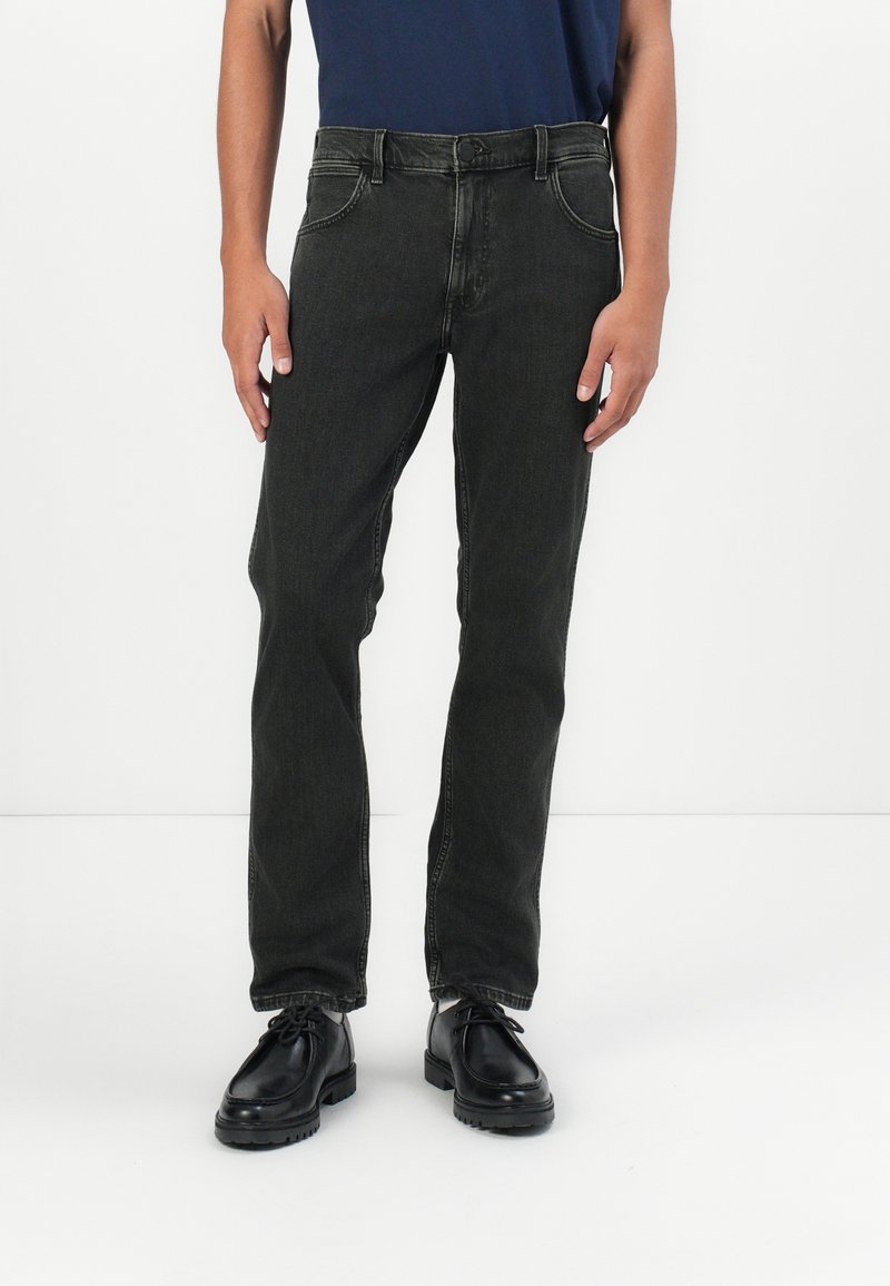 Jeans de mezclilla gris oscuro con corte recto, bolsillos frontales visibles y detalles cosidos, combinados con zapatos negros de cordones.