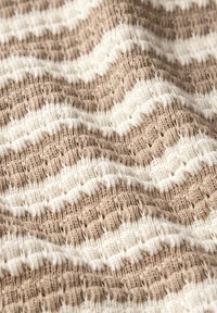 Gewebter Stoff mit einem gestreiften Muster in abwechselndem Beige und Creme, mit einer strukturierten Oberfläche und einem komplizierten Strickdesign.