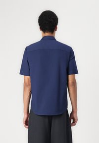 Camisa de manga corta azul marino con espalda recta, cuello clásico y dobladillo ligeramente curvado. El tejido parece ligero y transpirable.