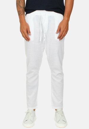 Pantaloni di lino bianchi con cintura elastica, dettaglio con cordino, vestibilità dritta e texture sottile, abbinati a sneaker bianche.