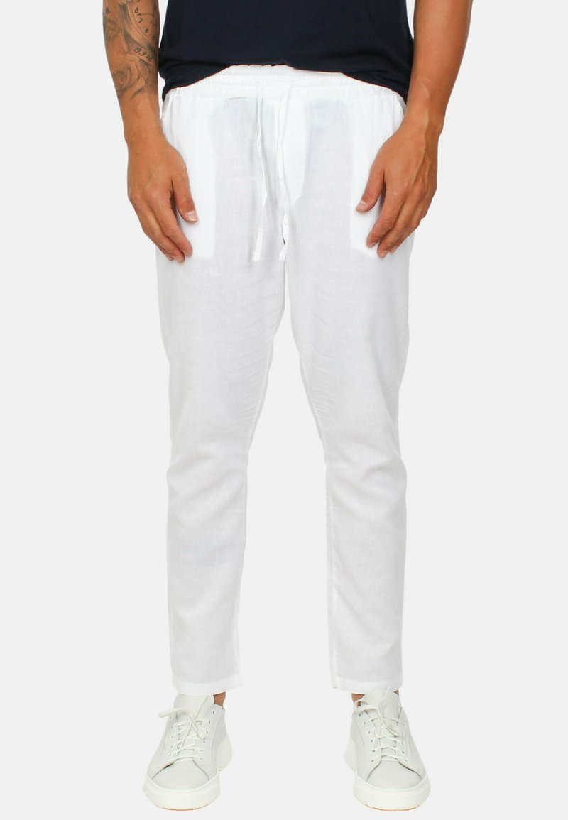 Pantaloni di lino bianchi con cintura elastica, dettaglio con cordino, vestibilità dritta e texture sottile, abbinati a sneaker bianche.