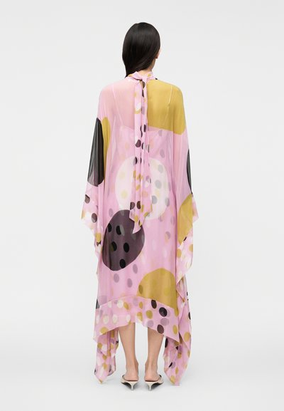 Priehľadný, voľne padajúci kaftan ružovej farby s veľkými farebnými kruhovými vzormi v čiernej, žltej a bielej farbe. Uviazaný pri krku, asymetrický lem.