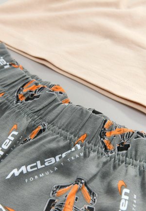 Pantalones cortos de tela gris con un patrón de McLaren Formula 1 en naranja y negro, y una cinturilla elástica. Una parte superior de color beige claro se encuentra detrás.