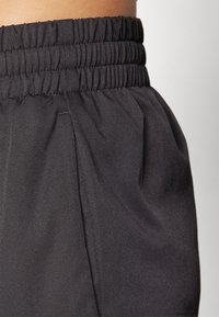 Close-up of black, elastic-waist trousers showing pleats and smooth fabric texture, highlighting their casual but stylish design.