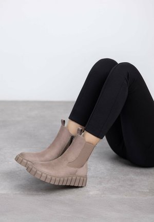 Botines de ante topo con paneles laterales elásticos, detalle de cremallera vertical y suela gruesa acanalada. Combinados con leggings negros.