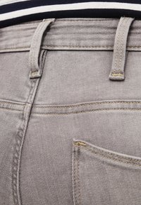 Los jeans de mezclilla gris cuentan con un diseño clásico de cinco bolsillos, costuras visibles y trabillas para el cinturón. Tienen una textura suave con un ligero estiramiento para mayor comodidad.