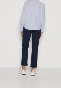 Blouse rayée bleu clair et blanc avec des manches bouffantes et des poignets froncés, associée à un jean bleu marine et des baskets blanches avec des accents jaunes.