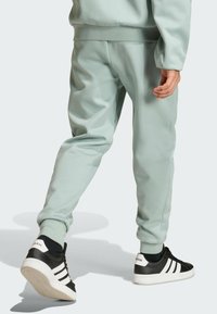 Light green sweatpants with a smooth texture, elastic cuffs, and two side pockets. Paired with black and white Adidas sneakers.