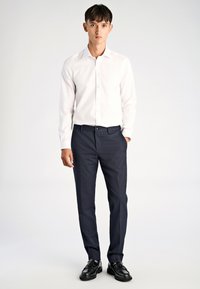 Weißes Hemd mit Knopfleiste, maßgeschneiderte dunkelblaue Hose und schwarze Schuhe. Glatter Stoff, schlichtes Design, eng anliegende Form und klassische Akzente.