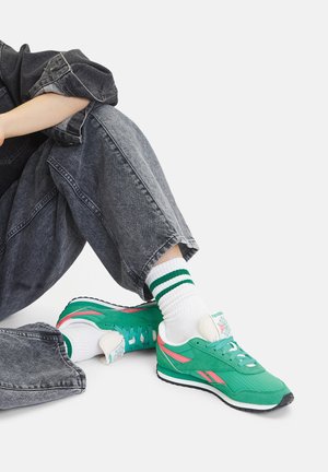 Zielone sportowe buty z siateczki z różowymi akcentami, białe podeszwy i kwiatowe logo. W zestawie z białymi skarpetkami z zielonymi paskami oraz szarymi dżinsami.