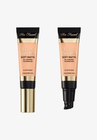 Fond de teint Soft Matte Born This Way de Too Faced dans deux tubes : un couleur pêche avec des accents dorés et noirs, l'un a un bouchon à pompe, l'autre un capuchon à rabat.