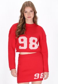 Rotes gestricktes zweiteiliges Set bestehend aus einem kurz geschnittenen Pullover und einem taillierten Rock, beide mit der weißen Zahl "98" versehen. Weicher Stoff, lässiges Design.