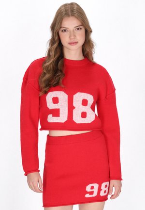 Set a due pezzi rosso in maglia composto da un maglione corto e una gonna aderente, entrambi con il numero bianco "98". Texture morbida, design casual.
