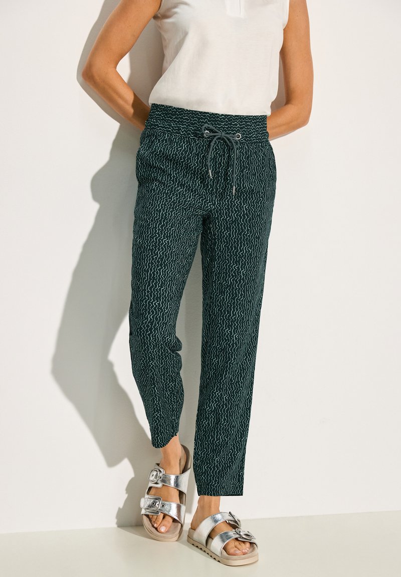 Patroon, donkergroene broek met een trekkoord in de taille, taps toelopende pijpen en een gestructureerd golvend ontwerp. Gepaarde met metallic sandalen.