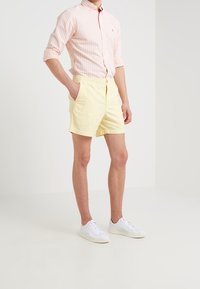 Světle žluté lněné šortky s elastickým pasem a postranními kapsami, kombinované s růžovou a bílou pruhovanou košilí na knoflíky a bílými teniskami.