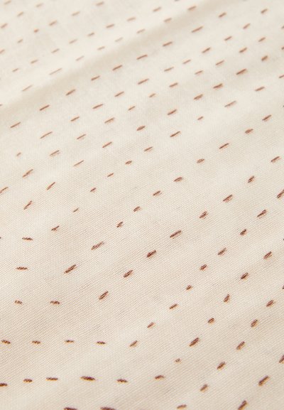 Baumwollstoff mit einem cremefarbenen Hintergrund, der mit kleinen braunen Punkten in einem sich wiederholenden Muster übersät ist, glatte Textur und weiche Oberfläche.