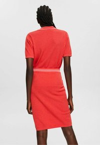 Punainen neulemekko lyhyillä hihoilla ja istuvalla muotoilulla, jossa on teksturoitu kangas ja kontrastoiva raidallinen vyötärö.