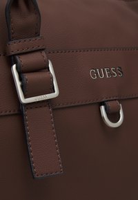 Sac à main en cuir marron avec une boucle et des accents en argent, logo gaufré et finition texturée sur un corps rectangulaire.