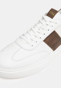 Sneakers bianchi in pelle liscia, con stripe in pelle marrone e colletto imbottito. Leggeri, suola in gomma e lacci piatti.