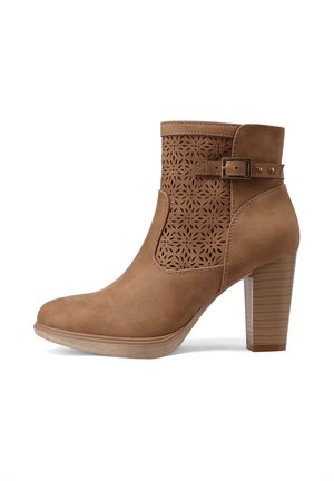 Stivaletto alla caviglia in camoscio color tabacco con tacco a blocco impilato, motivo floreale laserato e cinturino decorativo con fibbia su sfondo bianco.