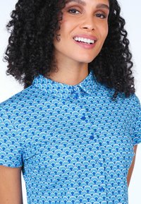 Short-sleeve shirt in a blue wave pattern. Button-up design with a collar; features light and dark blue accents. Smooth cotton texture.